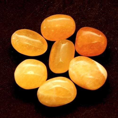 Oranje calciet trommelsteen van ca 2 x 1 cm uit Mexico