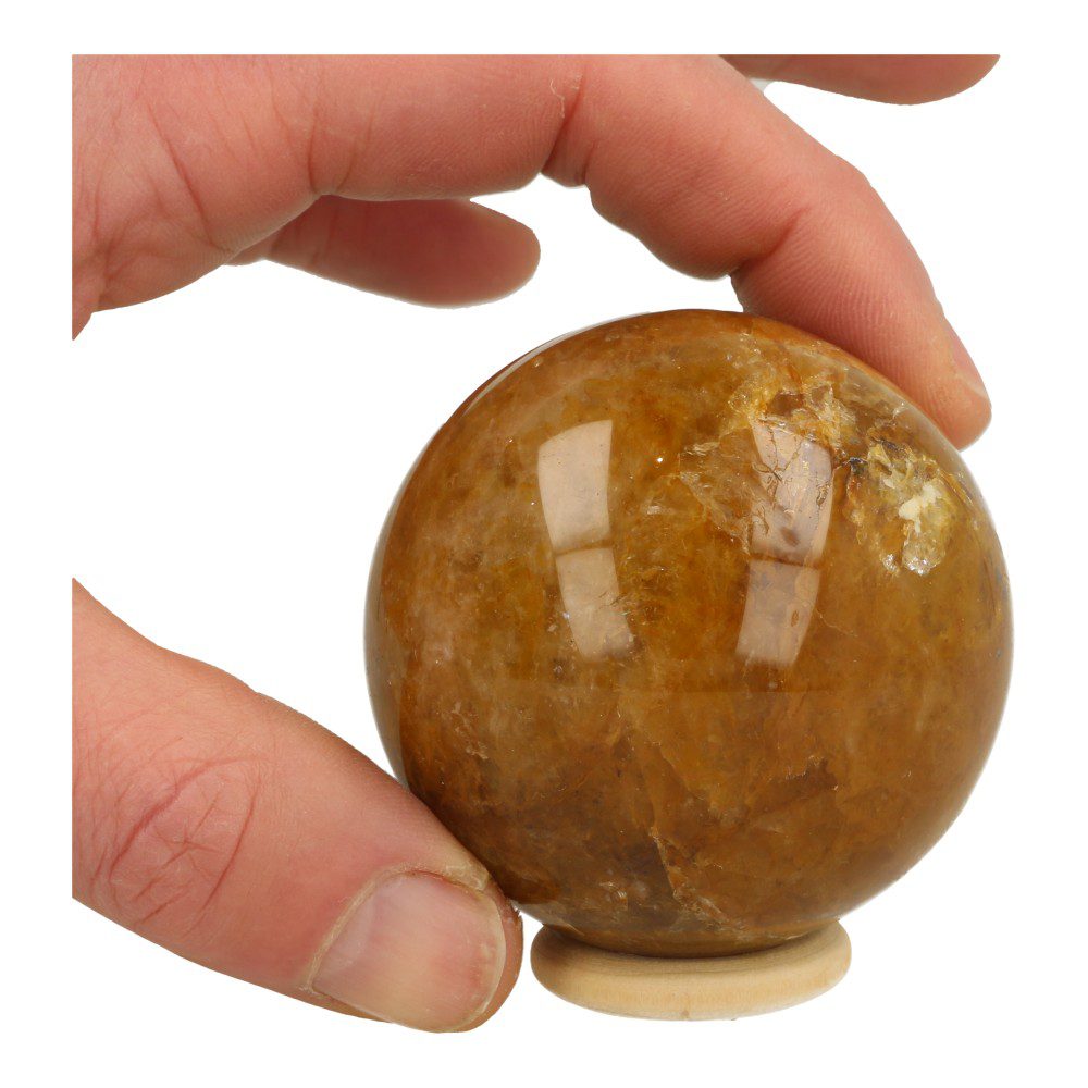 Overzichtsfoto in hand van fraaie donkere golden healer bol met diameter van ruim 63mm op houten ringetje