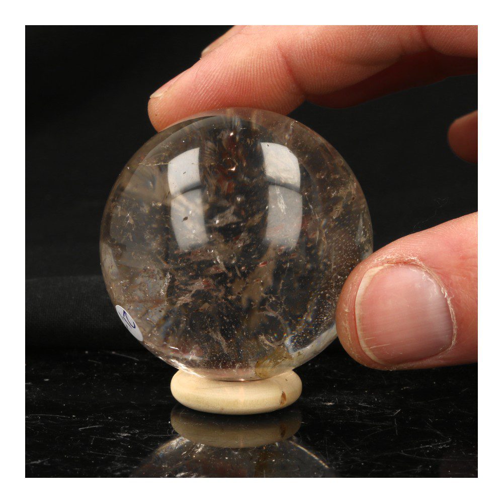 Helder bergkristal bol met diameter van 5cm en houten ring, detail in hand