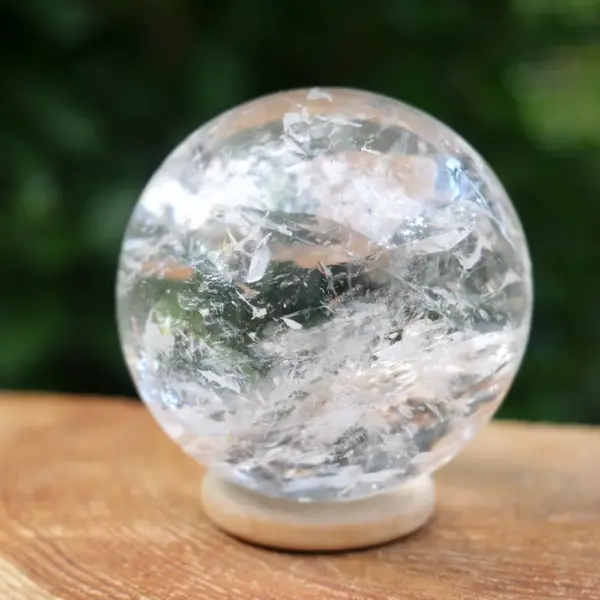 Zeer fraaie bergkristal bol met diameter van 56mm en vol regenboogjes op houten ring. Deze bol komt uit Brazilië